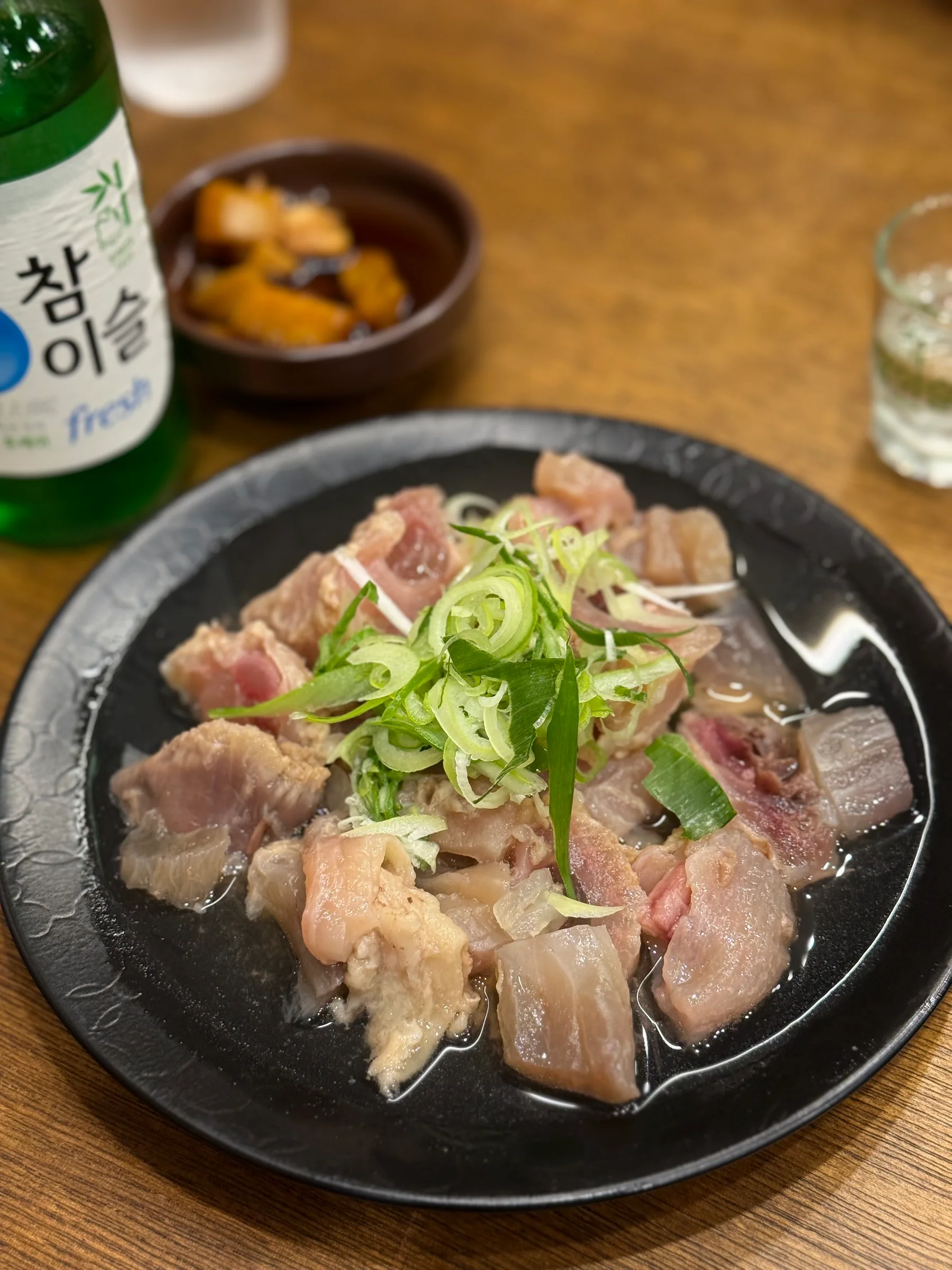 흑색 화형 접시에 담긴 소무관 모둠수육. 도가니와 아롱사태 위에 파채가 얹혀 있고 옆에 반주 한 병이 놓여 있다.